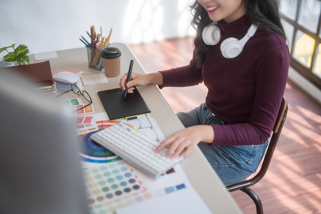 Foto freiberufliche grafikdesignerinnen tragen kopfhörer am hals, zeichnen logo-marken auf digitalen tablets und tippen auf dem computer, während sie mit technischen geräten im heimstudio an grafikdesign arbeiten.