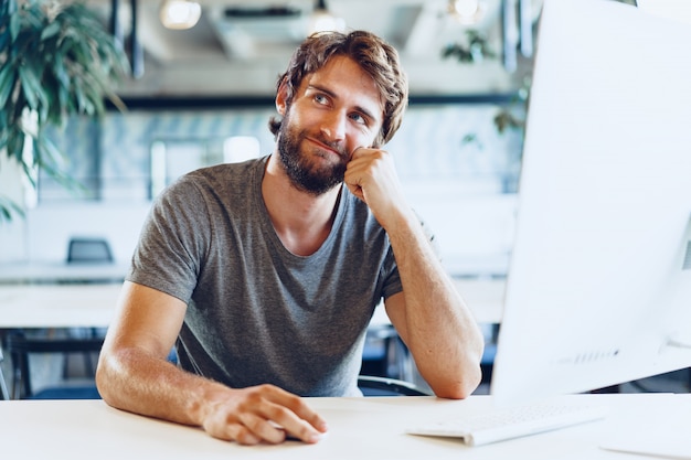 Freiberuflicher bärtiger Mann, der Computer in einem modernen Coworking Place verwendet. Freiberufliches Geschäftskonzept