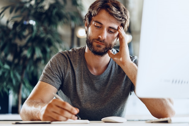 Freiberuflicher bärtiger Mann, der Computer in einem modernen Coworking Place verwendet