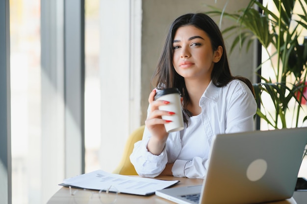 Freiberufliches Geschäfts- und E-Commerce-Konzept Kreative, begeisterte Journalistin, die neue Artikel schreibt, die auf dem Laptop lächelnde Abschreibungsprojektideen schreiben, sitzen im Café, trinken Kaffee und arbeiten fern