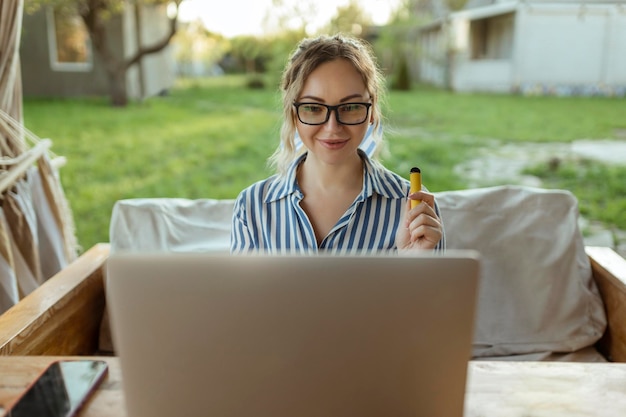 Freiberufliches Mädchen arbeitet an einem Computer und raucht vor dem Haus eine Elektrodenzigarette