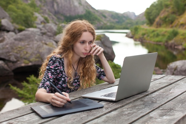 Freiberufliches Mädchen, das am Laptop in der Natur und in wunderschönen Landschaften arbeitet