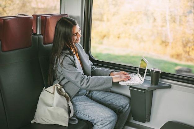 Foto freiberufliches mädchen, das mit einem laptop in einem zug sitzt. moderne technik und vernetzung.