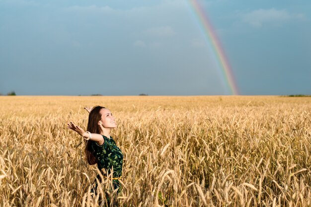 Freiheit. Frau mit offenen Händen auf Weizenfeld auf einem Hintergrund von Regenbogen