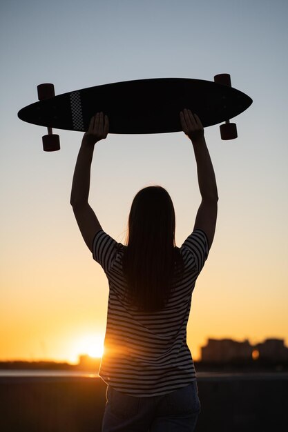 Freiheit und urbaner Lebensstil Teenager-Skater-Mädchen mit Longboard-Blick auf die Rückansicht des Sonnenuntergangs