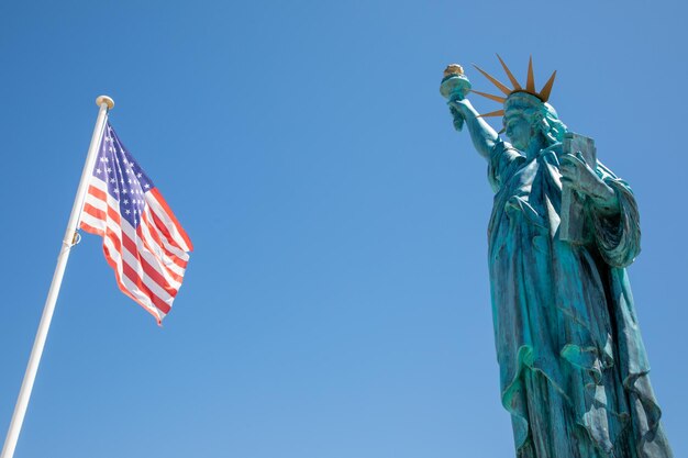 Foto freiheitsstatue mit us-amerikanischer flagge, die in einer matte mit wind am blauen himmel schwebt