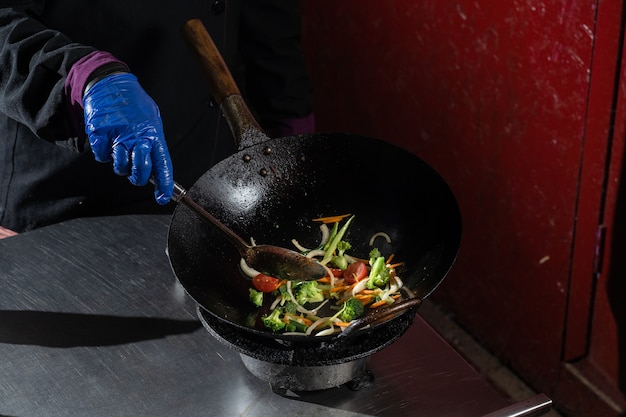 Foto freír verduras en una sartén wok cebollas, brócoli, tomates cherry, zanahoria, espárragos.