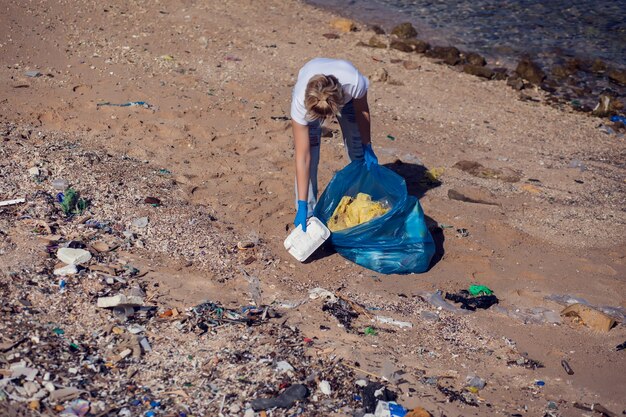 Freiwillige Frau mit großer blauer Tasche, die Müll am Strand sammelt. Konzept der Umweltverschmutzung