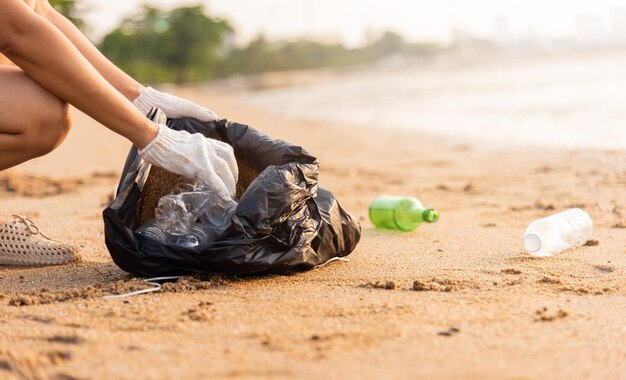 Freiwillige Frau pflückt Plastikflasche in Plastiktüte schwarz für die Reinigung des Strandes