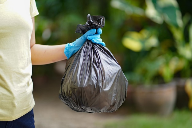 Freiwillige Wohltätigkeitsfrau, die schwarze Mülltüte und Plastikflaschenmüll zum Recycling für die Reinigung im Park hält, freiwilliges Konzept, Wiederverwendung und freiwillige Hilfe