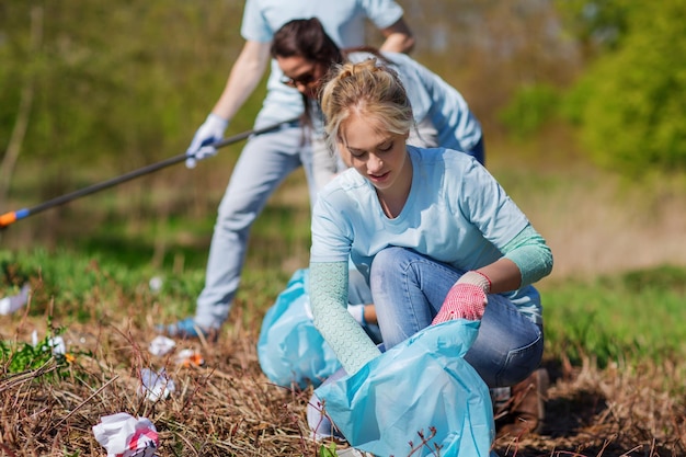 Freiwilligenarbeit, Wohltätigkeit, Reinigung, Menschen und Ökologiekonzept - Gruppe glücklicher Freiwilliger mit Müllsäcken im Park