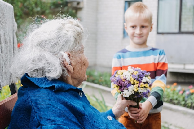 Freiwilliger Junge und ältere ältere Frau mit Geschenkblumenblumenstrauß und Lebensmittelkorb