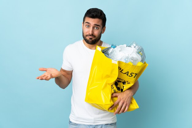 Freiwilliger junger kaukasischer Mann, der Recyclingbeutel über blauer Wand hält