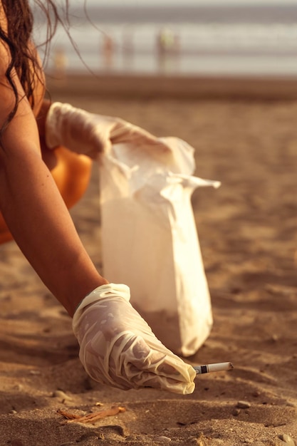 Freiwilliges Mädchen, das Zigarettenkippen auf dem Sand sammelt Meeresverschmutzung, die die Umwelt zerstört