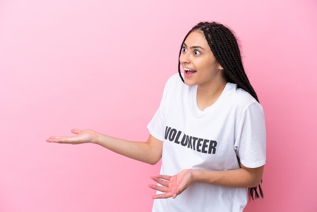 Freiwilliges Mädchen des Teenagers mit den Zöpfen lokalisiert auf rosa Hintergrund mit Überraschungsausdruck beim Schauen der Seite