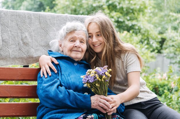 Freiwilliges Mädchen und ältere ältere Frau mit Geschenkblumenblumenstrauß und Lebensmittelkorb