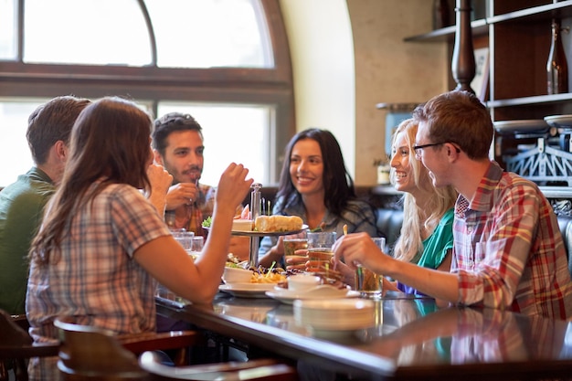 Freizeit-, Essens-, Getränke-, Menschen- und Urlaubskonzept - glückliche Freunde, die in einer Bar oder Kneipe essen und trinken