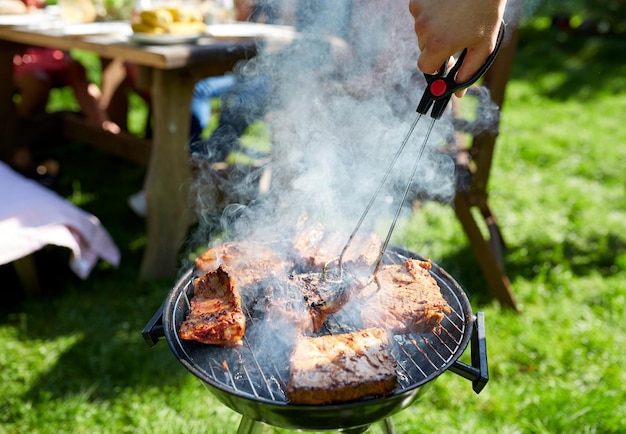 Freizeit-, Essens-, Menschen- und Urlaubskonzept - Mann kocht Fleisch auf dem Grill für seine Freunde auf einer Sommerparty im Freien