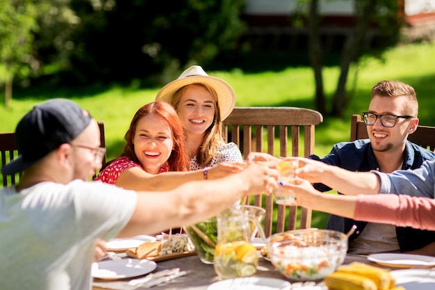 Freizeit, Feiertage, Essen, Menschen und Essenskonzept - glückliche Freunde, die Gläser anstoßen und bei der Sommergartenparty feiern