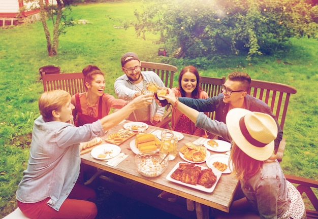 Freizeit, Feiertage, Essen, Menschen und Essenskonzept - glückliche Freunde, die Gläser anstoßen und bei der Sommergartenparty feiern