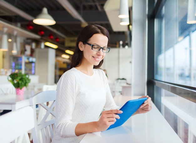 Freizeit-, Geschäfts-, Menschen-, Technologie- und Lifestyle-Konzept - lächelnde junge Frau mit Brille und Tablet-PC-Computer im Café