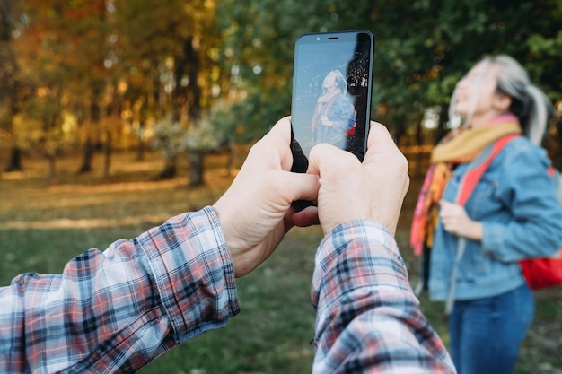 Freizeit im Herbst Mann mit Smartphone-Kamera, um ein Foto seiner Freundin auf dem Hintergrund des Naturparks im Herbst zu machen