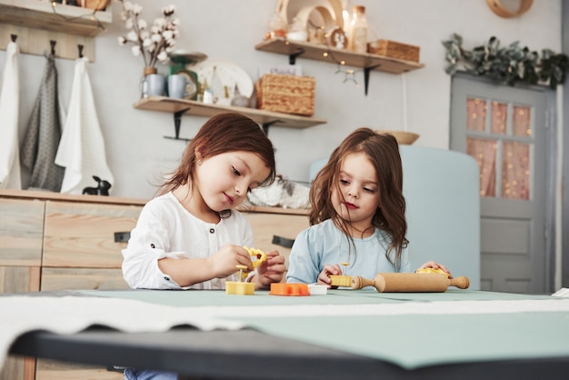 Freizeit, in der die Eltern nicht zu Hause sind. Zwei Kinder, die mit den gelben und orange Spielwaren in der weißen Küche spielen