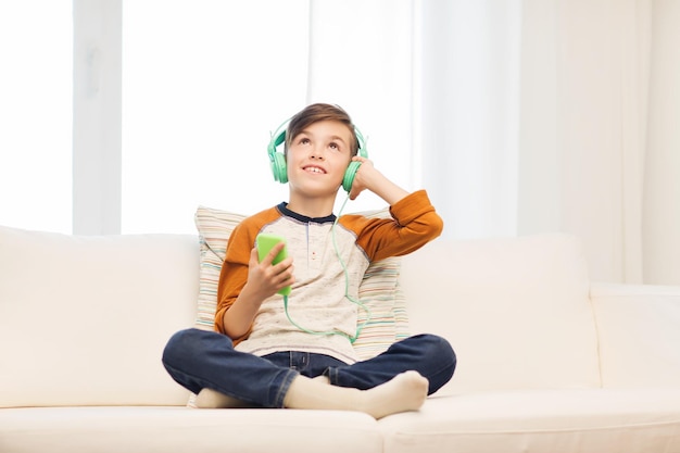 Freizeit-, Kinder-, Technologie- und Personenkonzept - lächelnder Junge mit Smartphone und Kopfhörern, der zu Hause Musik hört