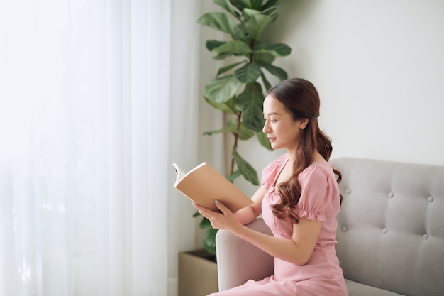 Freizeit-, Literatur- und Menschenkonzept - lächelnde asiatische Frau, die zu Hause ein Buch liest