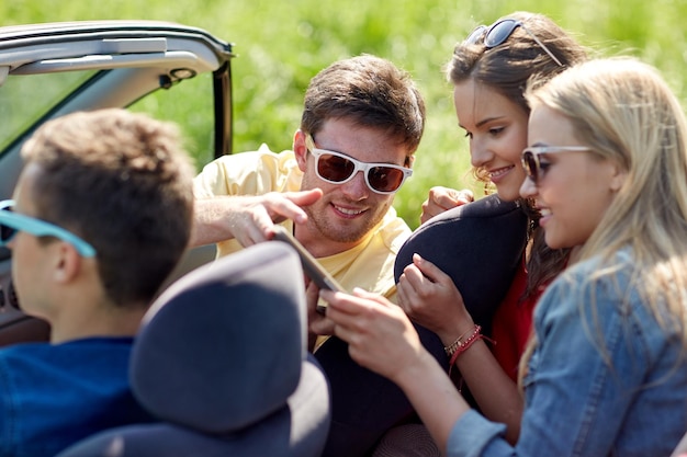 freizeit-, roadtrip-, reise-, technologie- und personenkonzept - glückliche freunde mit tablet-pc-computer, der im cabriolet-auto entlang der landstraße fährt