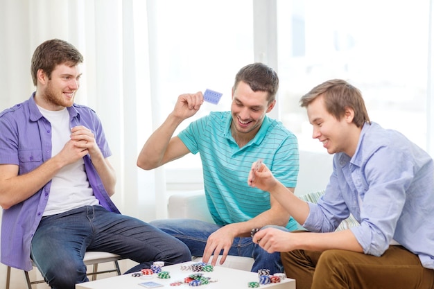 Freizeit-, Spiele- und Lifestyle-Konzept - glückliche drei männliche Freunde, die zu Hause Poker spielen