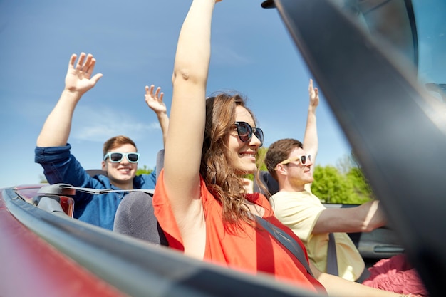 Freizeit-, Straßenreise-, Reise- und Personenkonzept - glückliche Freunde, die im Cabriolet-Auto auf dem Land fahren und Spaß haben