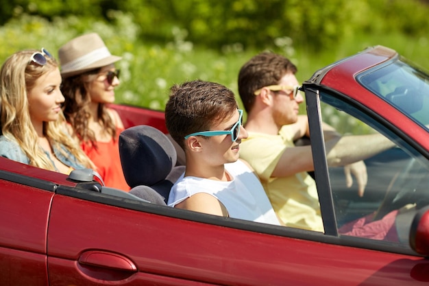 Freizeit-, Straßenreise-, Reise- und Personenkonzept - glückliche Freunde, die im Cabriolet-Auto entlang der Landstraße fahren