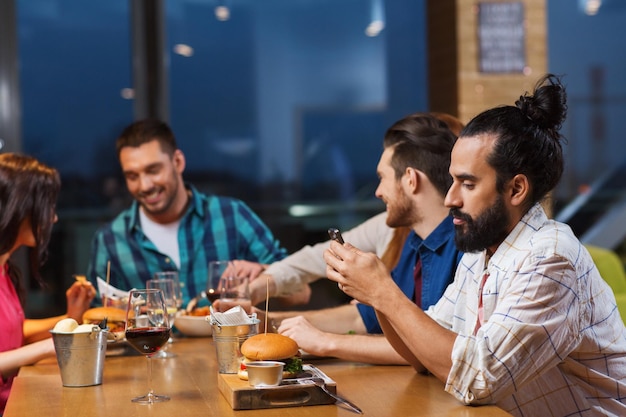 Freizeit, Technologie, Internetsucht, Lifestyle und Personenkonzept - Mann mit Smartphone und Freunden im Restaurant