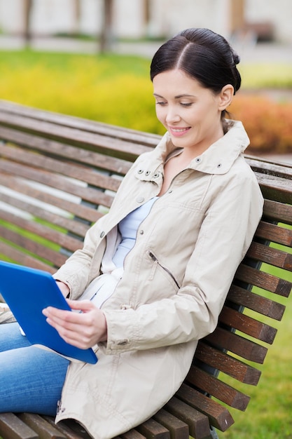 freizeit-, technologie-, kommunikations- und menschenkonzept - lächelnde frau mit tablet-pc-computer, die auf einer bank im park sitzt