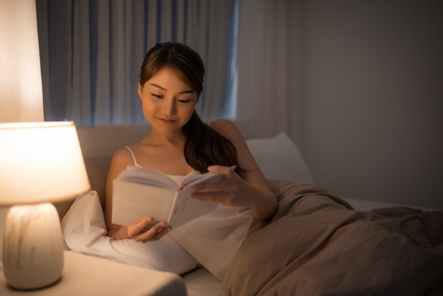 Freizeit- und Menschenkonzept - junge Frau, die nachts ein Buch im Bett liest