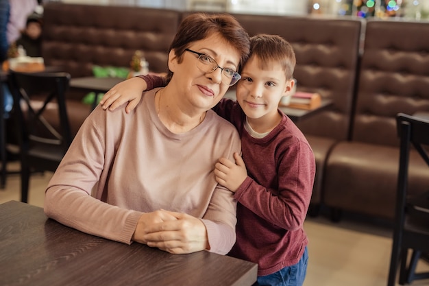 Freizeit und unterhaltung für familien. glückliche großmutter mit kurzen haaren, brille und enkel ruhen sich in einem café aus. kind umarmt großmutter