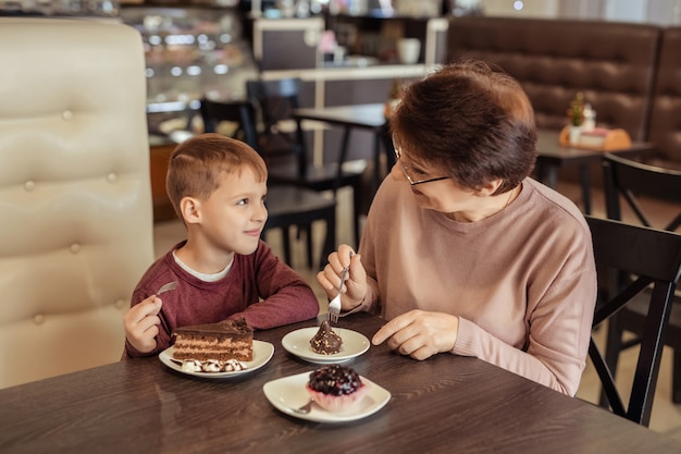 Freizeit und Unterhaltung für Familien. glückliche Großmutter mit kurzen Haaren, Brille und Enkel ruhen sich in einem Café aus. Sie essen Kuchen mit Milchshakes