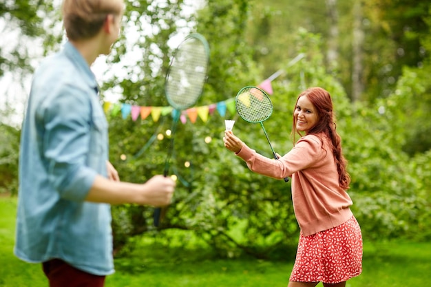 Freizeit-, Urlaubs-, Menschen- und Sportkonzept - glückliches Paar oder Freunde, die im Sommergarten Badminton oder Federball spielen