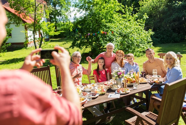 Foto freizeitferien und menschenkonzept glückliche familie, die ein festliches abendessen oder eine sommergartenfeier veranstaltet und mit dem smartphone fotografiert