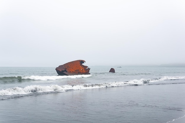 Fremains de naufragio oxidado de un barco arrastrado a tierra contra un paisaje marino brumoso