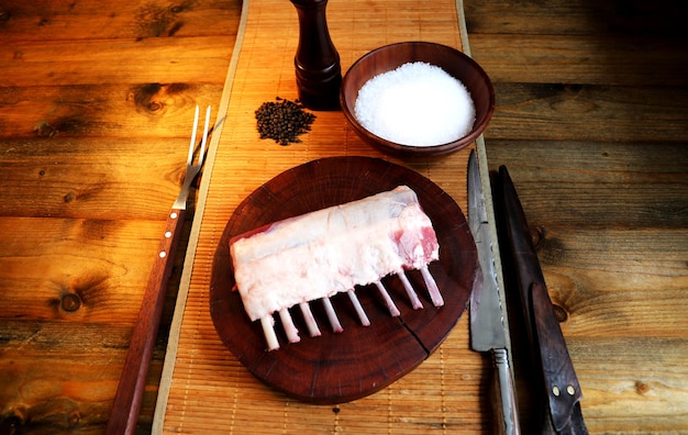 French Rack Rohe Lammstücke geschnitten auf einem Holzbrett mit Salz und Pfeffer im Hintergrund