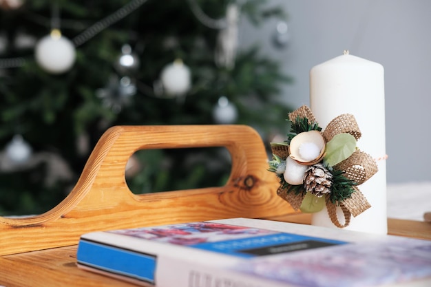 Frente al árbol de Navidad hay una bandeja con una vela decorada y un libro.