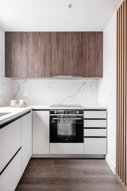 Frente de una cocina con muebles de madera blanca con cajones y muebles de madera altos paredes de mármol blanco y listones de madera