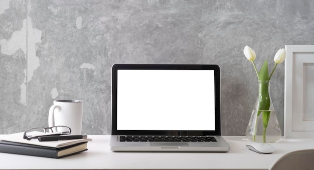 Frente com computador portátil com livros de moldura de tela branca vazia e xícara de café na mesa branca Local de trabalho elegante