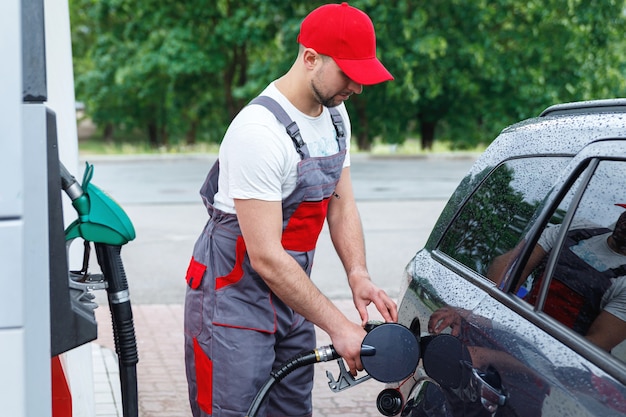 Frentista do posto de gasolina com um bico de combustível nas mãos, enchendo o tanque do carro do cliente