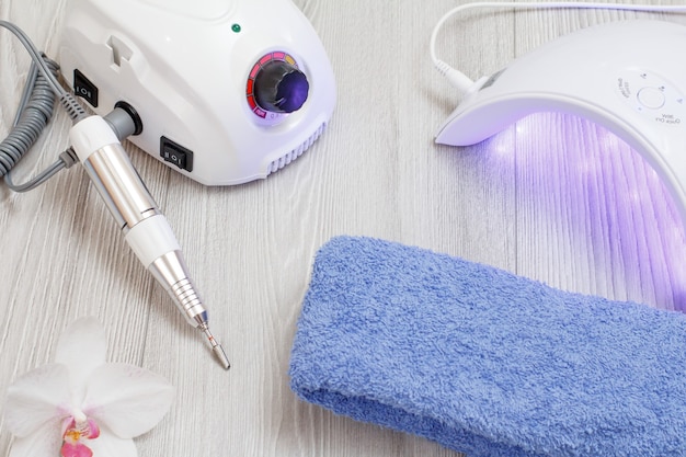 Fresa, acesa lâmpada ultravioleta led e toalha com flor de orquídea em fundo cinza de madeira. Um conjunto de ferramentas cosméticas para manicure profissional de hardware. Vista do topo