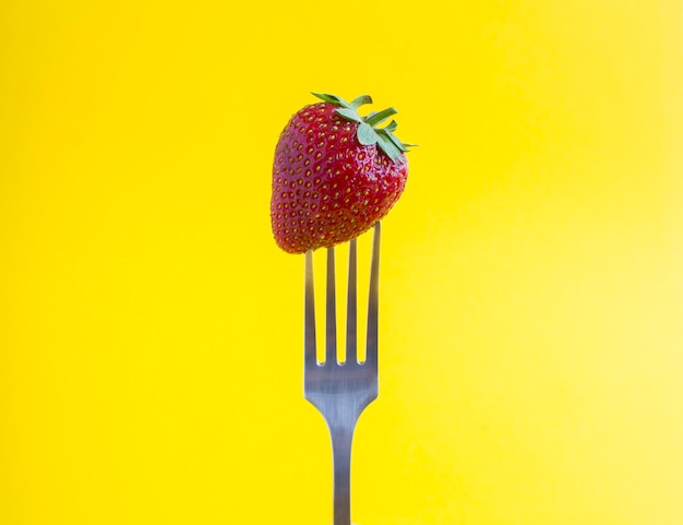 Fresa apuñalada en un tenedor de plata sobre el fondo amarillo Primer plano