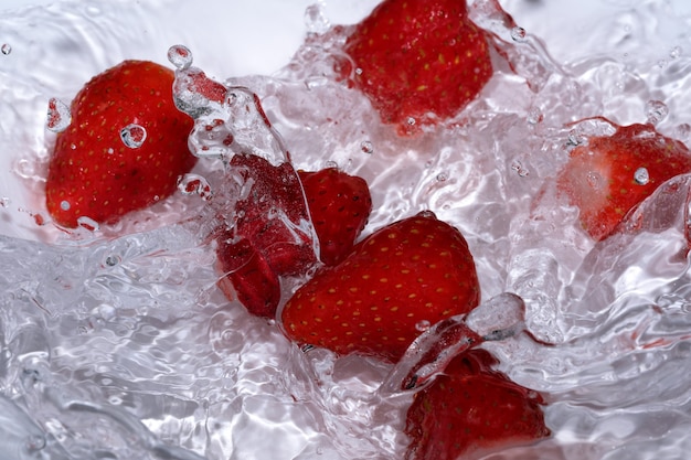 Fresa fresca dulce madura se lava en agua fría limpia con salpicaduras y burbujas de cerca