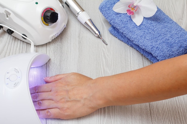 Fresa y lámpara UV led para secar las uñas de la mujer sobre fondo de madera gris. Un conjunto de herramientas cosméticas para manicura de hardware profesional. Vista superior.